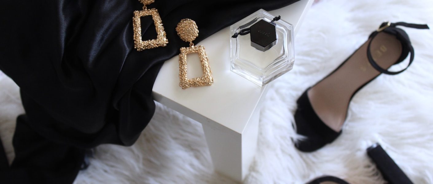 pair of gold-colored earrings on table and black ankle-strap pumps on area rug